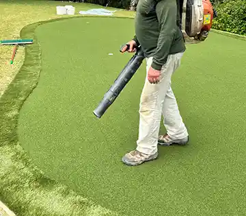 image of synthetic golf putting green being cleaned with a leaf blower